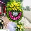 Vòng hoa chia buồn - Cõi Tạm gồm hoa lan trắng, tím, vàng, hoa ly.